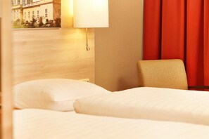 Ein Hotelzimmer mit einem Bett, einem Sessel, einer Lampe und einem an der Wand hängenden Bild.