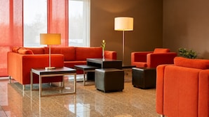 Un vestíbulo moderno con sofás naranja, una mesa de centro, una lámpara de pie y una planta en maceta.