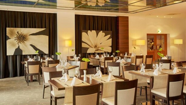 Un comedor de hotel con mesas dispuestas para los huéspedes, grandes pinturas florales en las paredes y un diseño de techo moderno.
