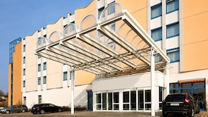 Un edificio moderno con acceso cubierto, múltiples ventanas y coches estacionados.