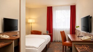 Habitación de hotel con cama, dos sillas, escritorio con teléfono, televisor y lámpara.