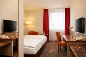 A hotel room with a bed, two chairs, a desk with a telephone, a television, and a lamp.