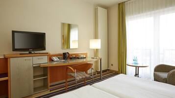 Une chambre d’hôtel comprenant un lit, un bureau avec une télévision, une chaise, une lampe et une petite table avec des bouteilles d’eau.