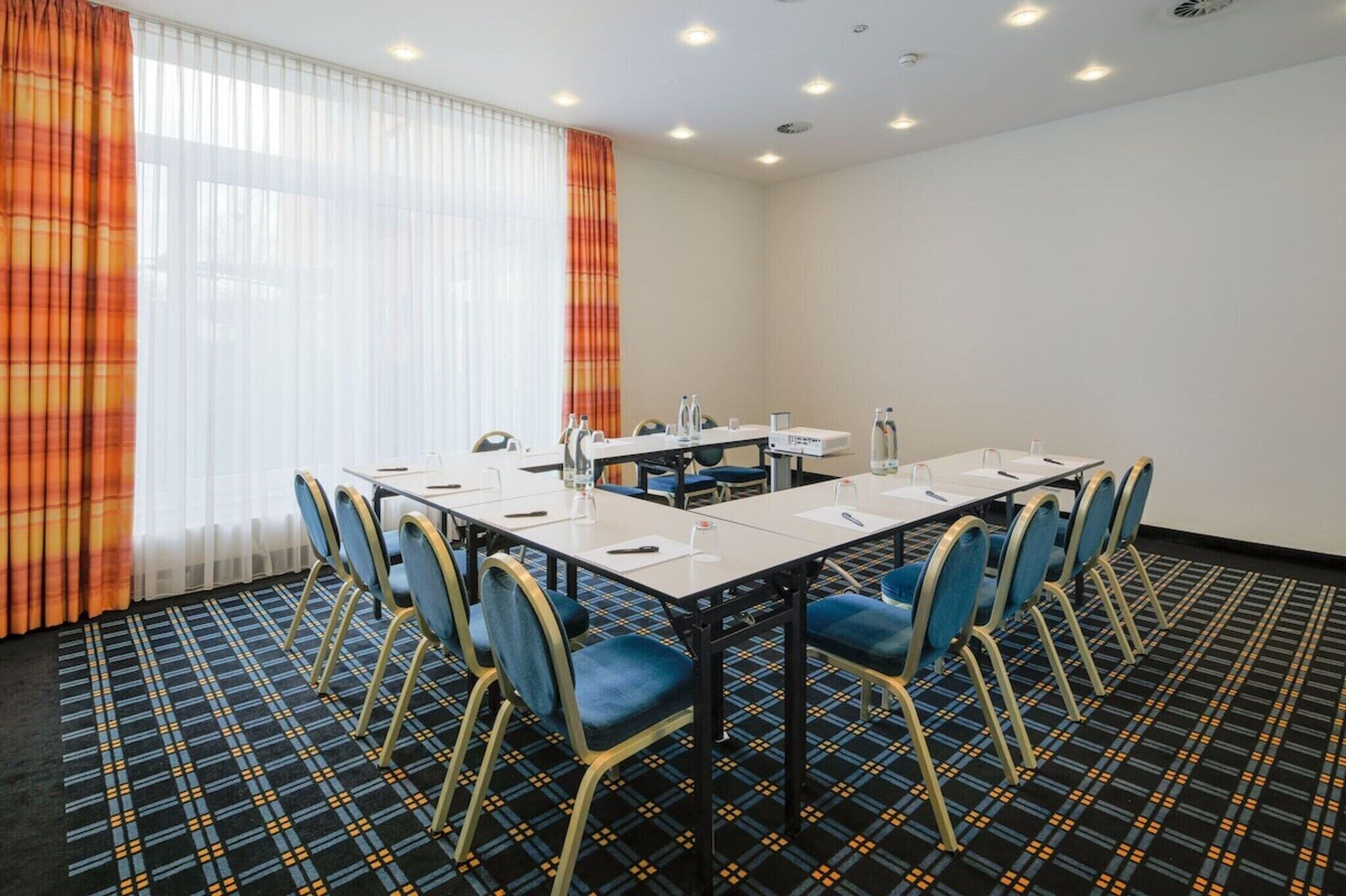 A conference room with a long table, chairs, and a window with curtains.