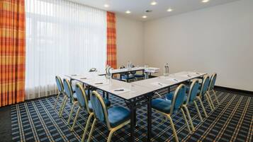 A conference room with a long table, chairs, and a window with curtains.