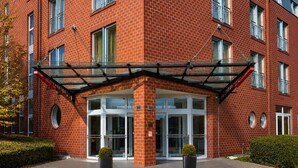 A red brick building with a glass entrance, two potted plants, and a metal awning. - Sunday Hotel Köln Hürth Single Room (Hürth)