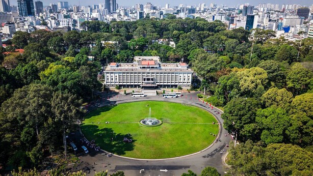 An aerial view of a cityscape with a large building surrounded by greenery, a circular park, and a fountain.