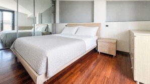 Une chambre moderne avec un grand lit, une table de chevet en bois, une commode et une porte-fenêtre coulissante donnant sur un balcon.