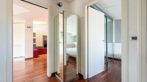 Un intérieur moderne avec un plancher en bois, un lit, un canapé rouge et un coin cuisine visible à travers une porte ouverte.