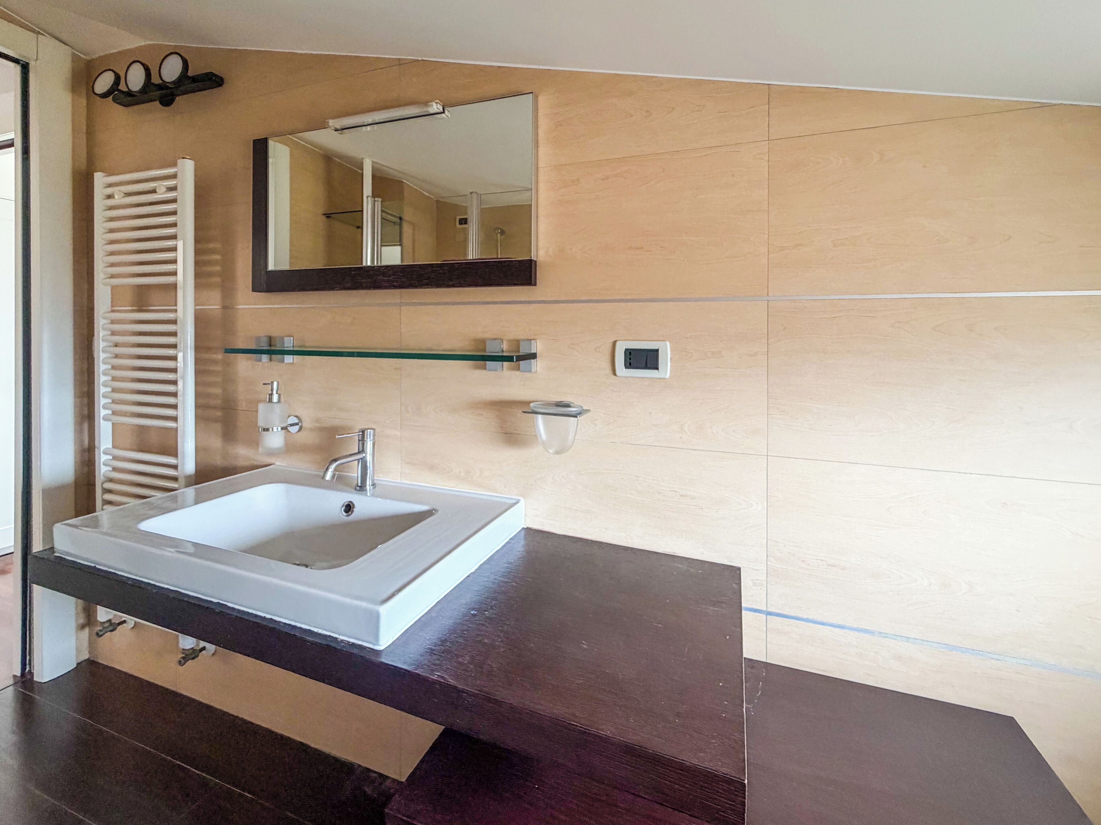 A bathroom with a white sink, a mirror, a towel rack, and a glass shelf.