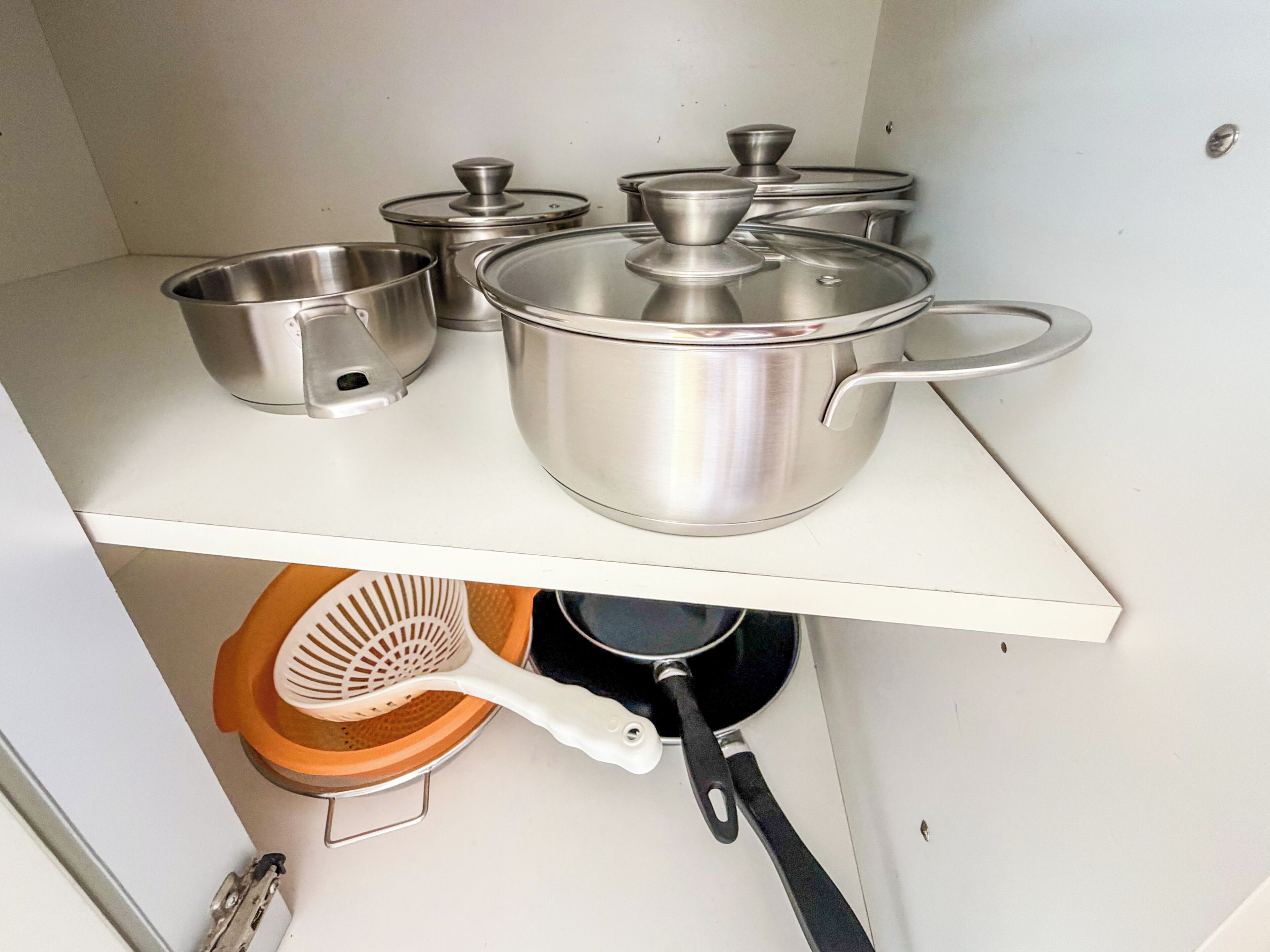 A kitchen with stainless steel cookware, including pots and pans, on a white countertop.