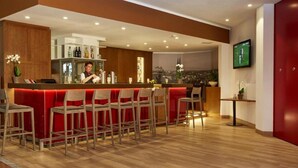 Eine Bar mit einem Barkeeper, Holzstühlen, einer roten gepolsterten Bar und Blick auf die Stadt.