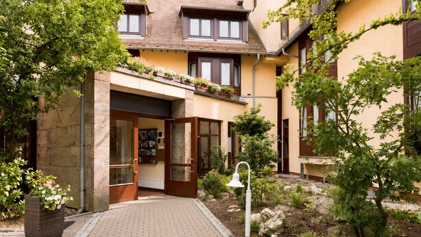 Ein Innenhof mit einem Hauseingang, einer Topfpflanze und einer Lampe.