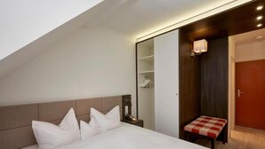 Ein Hotelzimmer mit einem Bett, einem Nachttisch mit Lampe, einer kleinen Bank und einem Kleiderschrank.