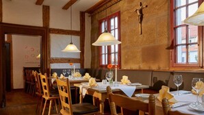 Ein Essbereich mit Holztischen und -stühlen, Pendelleuchten und einem Kruzifix an der Wand.