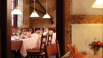 A restaurant interior with wooden chairs, tables set with white tablecloths, and hanging pendant lights.