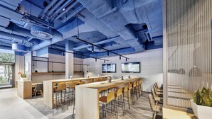 A modern office space with a long communal table, individual workstations, and a large screen on the wall.