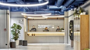 A reception area with a modern design, featuring a reception desk, three staff members, and a large potted plant.