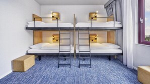 A hotel room with bunk beds, a window with curtains, and a view of the city.