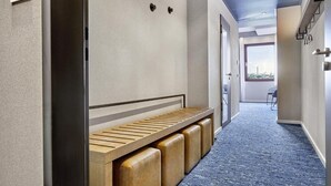 A hallway with a bench, a door with a number, and a view to the outside.
