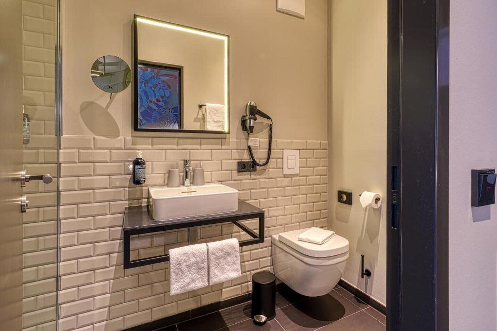 Un baño moderno con lavamanos, espejo y inodoro blancos, con salpicadero de azulejos y cabina de ducha de cristal.