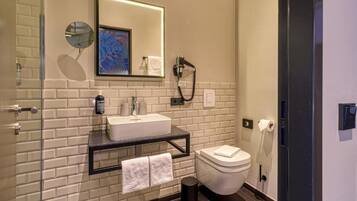 Un baño moderno con lavamanos, espejo y inodoro blancos, con salpicadero de azulejos y cabina de ducha de cristal.