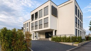A modern building with a flat roof, large windows, and a paved entrance area. - Sunday Hotel Bonn Standard Room (Bonn)