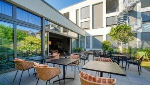 An outdoor patio area with tables and chairs, a staircase, and a building with large windows and balconies. - Sunday Hotel Bonn Standard Room (Bonn)