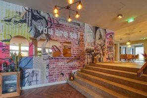 A staircase with a colorful mural, a wooden cabinet with decorative items, and a seating area with a table and chairs.
