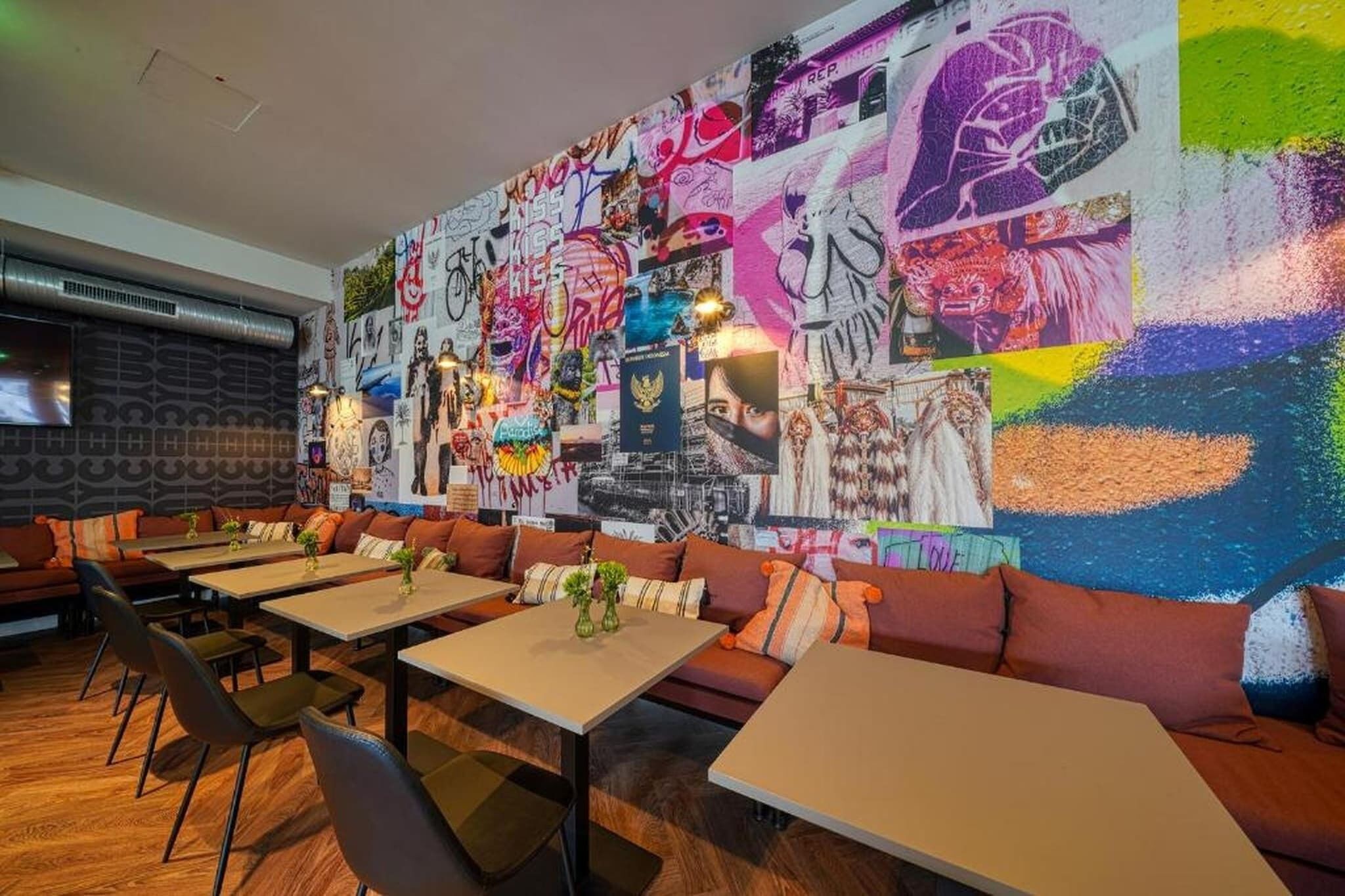 Un restaurante con un mural llamativo, piso de madera y asientos modernos.