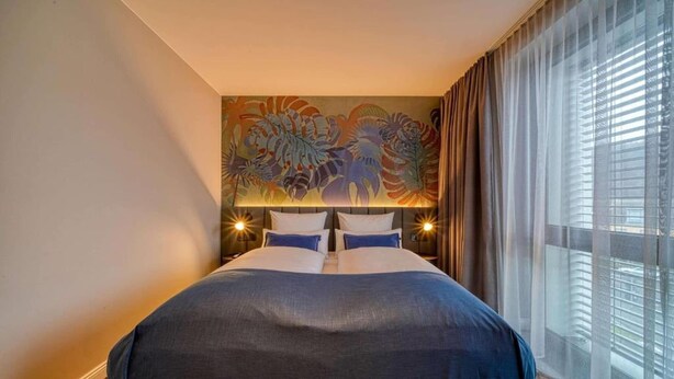 A hotel room with a large bed, a painting on the wall, and a window with curtains. - Sunday Hotel Bonn Standard Room (Bonn)