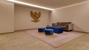 Habitació amb una paret beix, un sofà marró, dos otomans blaus i un emblema vermell i blanc a la paret.