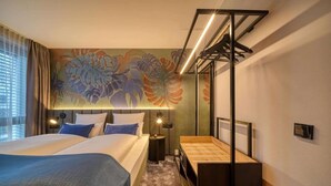 Una habitació d'hotel amb un llit gran, una taula de treball, una cadira, un mirall i una paret amb un mural floral.