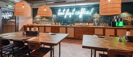 A modern cafe with wooden tables and chairs, a neon sign, and a bar area.