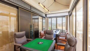 A billiards room with a pool table, leather chairs, and large windows offering a view of the city.