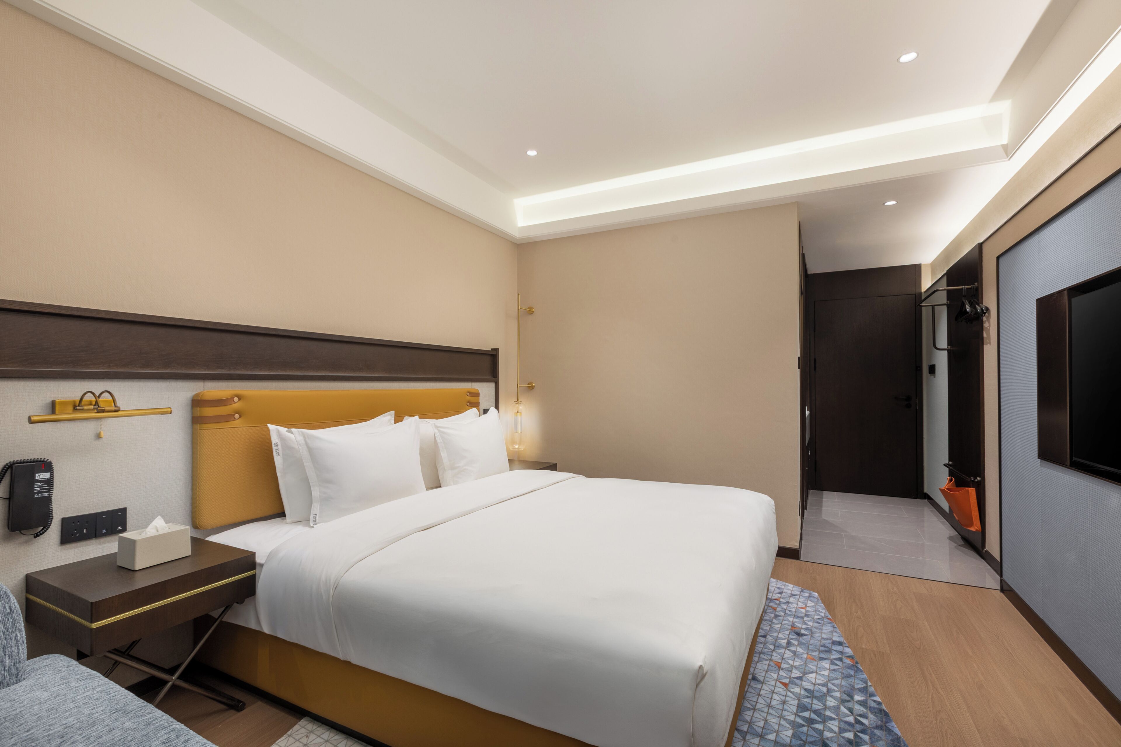 Ein Hotelzimmer mit Bett, Nachttisch, Lampe und Fernseher.