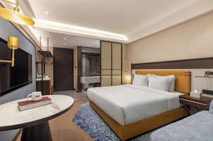 Habitación de hotel moderna con una cama grande, mesitas de noche, una mesa redonda, televisión y un baño visible a través de una puerta de vidrio.