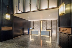Un hall de hotel con mostrador de recepción, quiosco informativo digital y una pared decorativa con diseño geométrico.