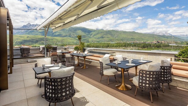 Une terrasse extérieure, dotée de tables et de chaises, qui offre une vue sur un paysage montagneux.