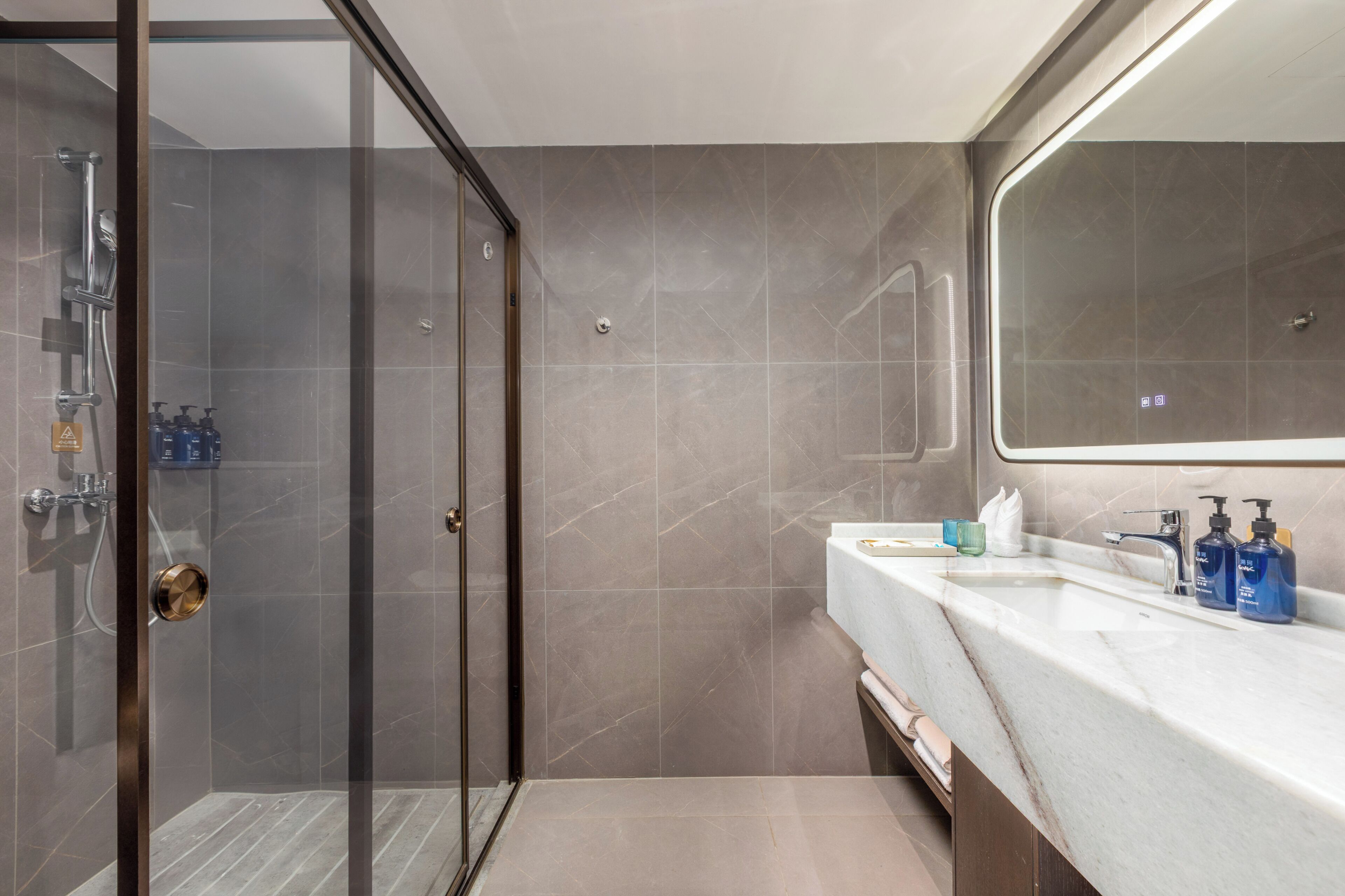 Un baño moderno con cabina de ducha de vidrio, lavamanos de mármol y un espejo grande.