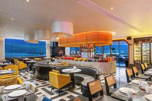 Un moderno vestíbulo de hotel con zona de bar, espacios de descanso y vistas amplias por grandes ventanales.