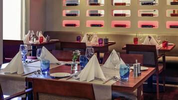 Ein Restaurant mit mehreren für den Genuss gedeckten Tischen, jede mit weißer Tischdecke, Besteck und blauem Glas.
