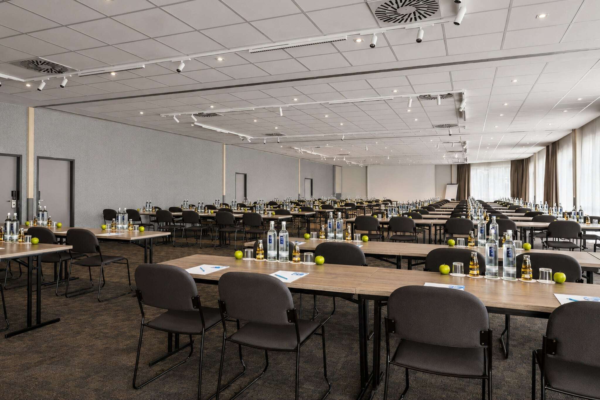 Una grande sala conferenze con numerosi tavoli, sedie e una lunga fila di finestre.