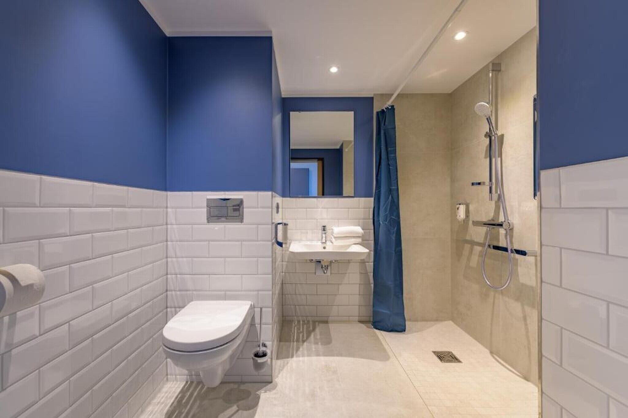 Un baño moderno con azulejos blancos, inodoro, lavabo y ducha.