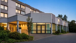 A modern hotel with a flat facade, large windows, and a well-lit entrance. - Sunday Hotel Kelsterbach Twin Room (Kelsterbach)
