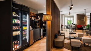 A modern hotel lobby with a refrigerator stocked with beverages, a wooden accent wall, and a seating area with tables and chairs. - Sunday Hotel Kelsterbach Twin Room (Kelsterbach)