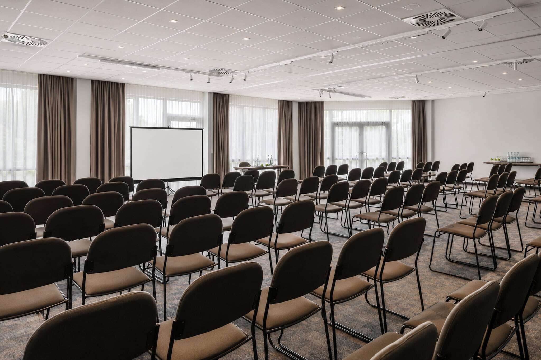 A conference room with rows of chairs, a projector screen, and a table with water bottles.