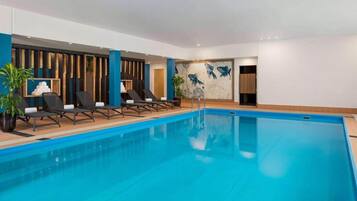 A modern indoor pool area with lounge chairs, a wooden floor, and a wall with a fish mural.