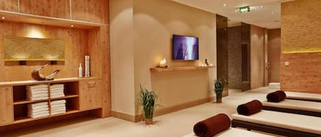 A spa room with wooden paneling, a television, massage tables, and a shelf with towels.