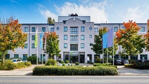 Un hotel moderno con fachada simétrica, varias banderas y un jardín cuidado.